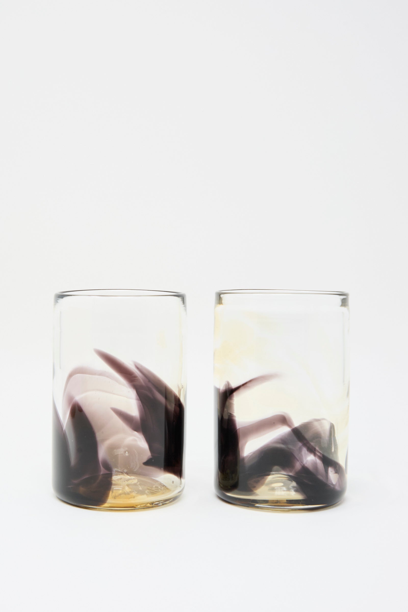Two Hand Dyed Fumé Glass tumblers by Upstate, featuring clear hand-blown glass with abstract black and beige swirls on the lower half, set against a plain white background.