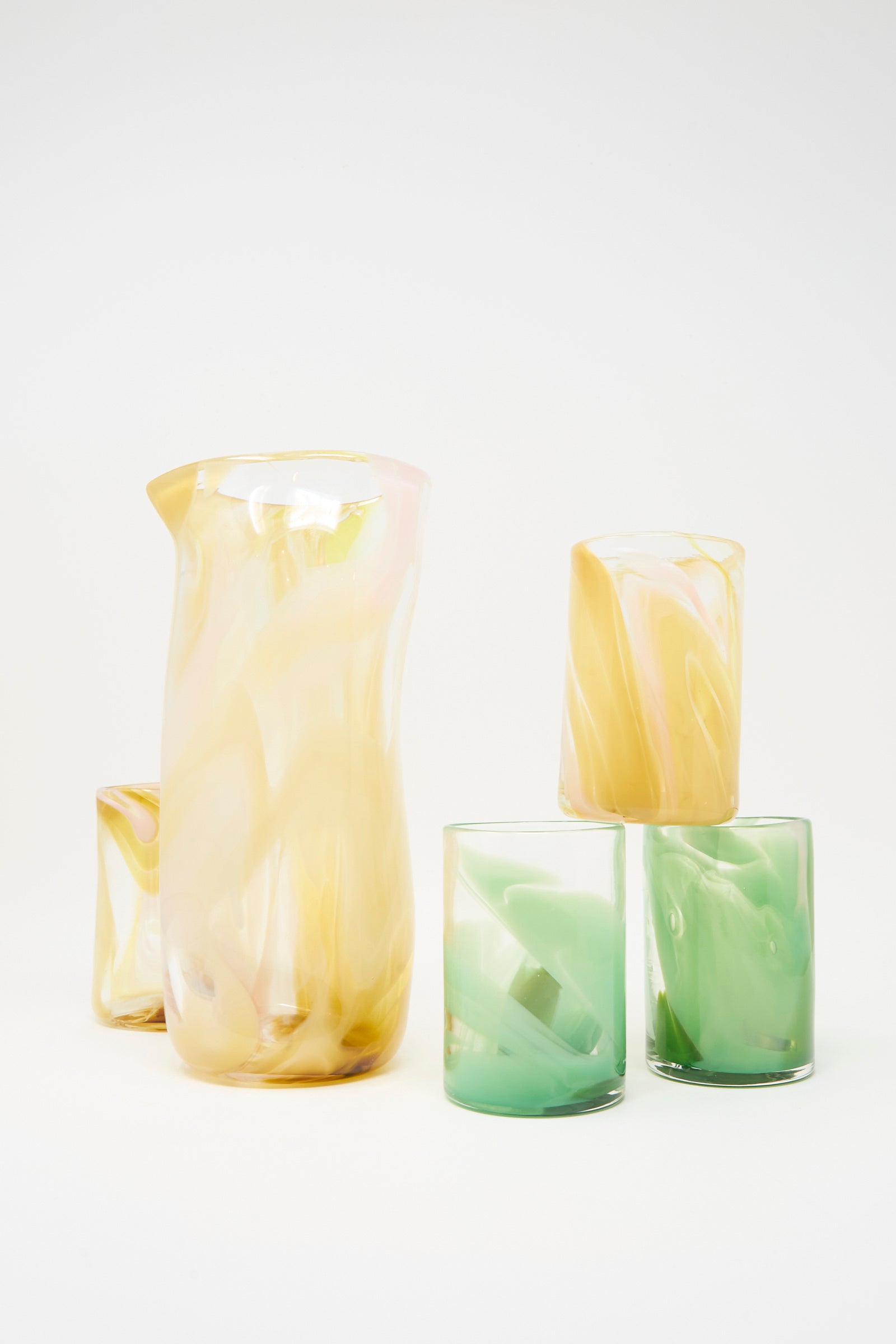 The Upstate Hand Dyed Moss Glass set includes one pitcher and four hand-blown tumblers in abstract swirled pastel yellow, green, and white, handmade in NYC and shown on a white background.