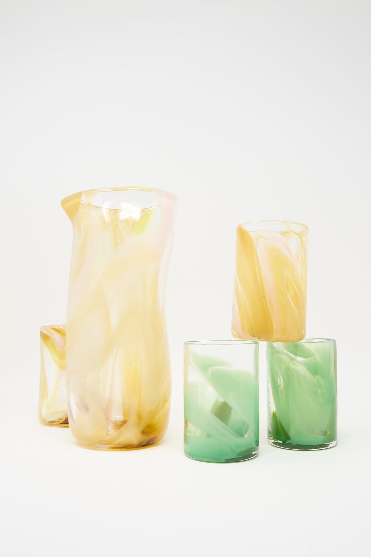 The Gone Hand Dyed Moss Glass set includes one pitcher and four green glass tumblers with pastel yellow and green swirls, all handmade in NYC, displayed on a white background.