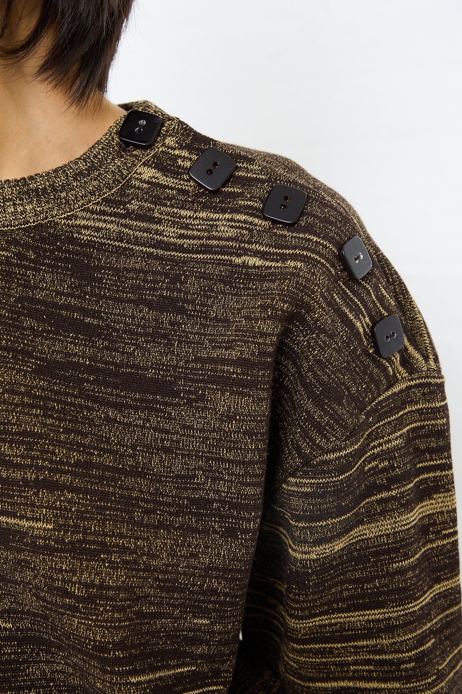 Close-up of a person wearing a Veronique Leroy Cotton Boxy Sweater in Pepper with decorative buttons on the shoulder.