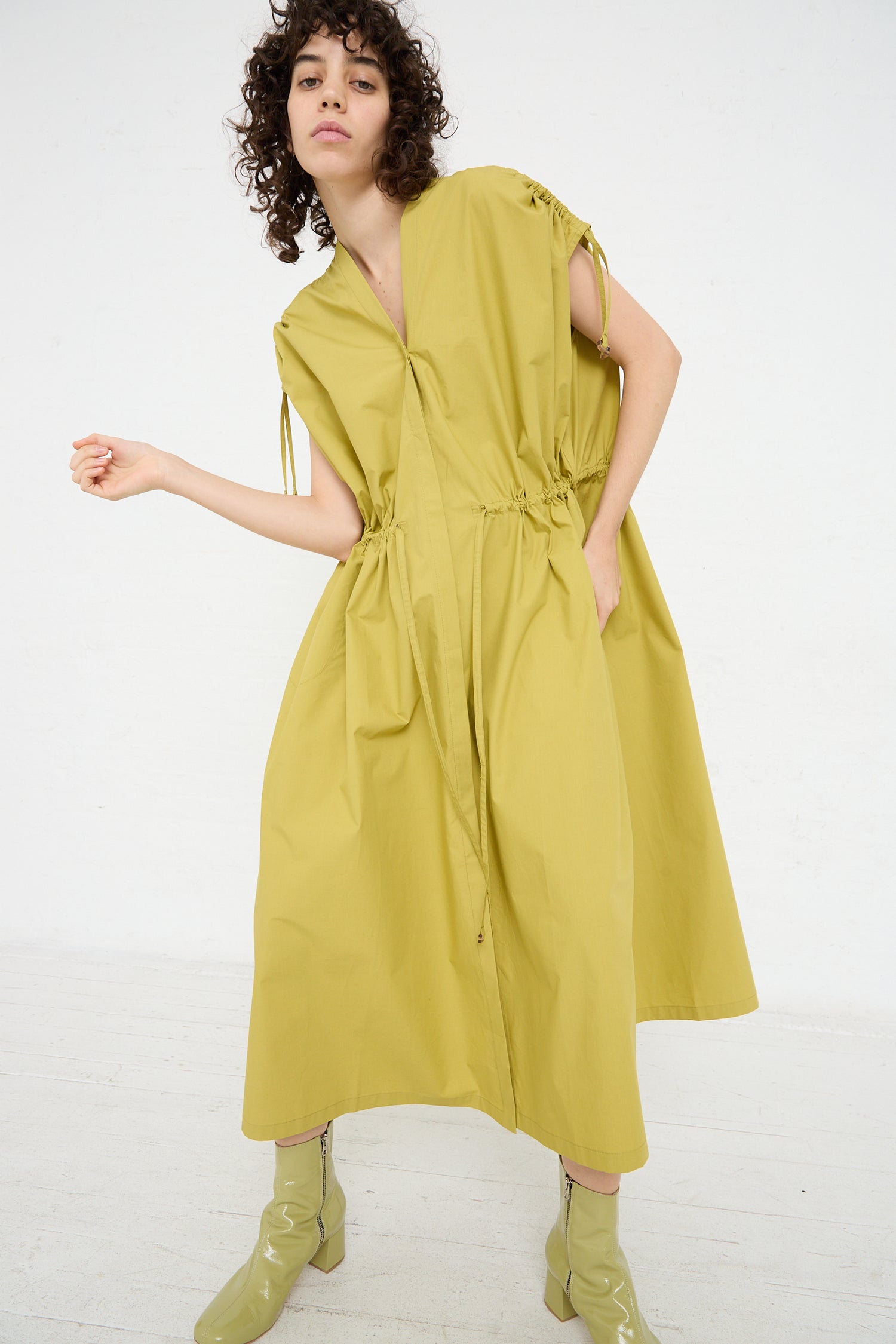 The model is wearing an oversized yellow Veronique Leroy Cotton Poplin Gathered Dress in Matcha and boots.