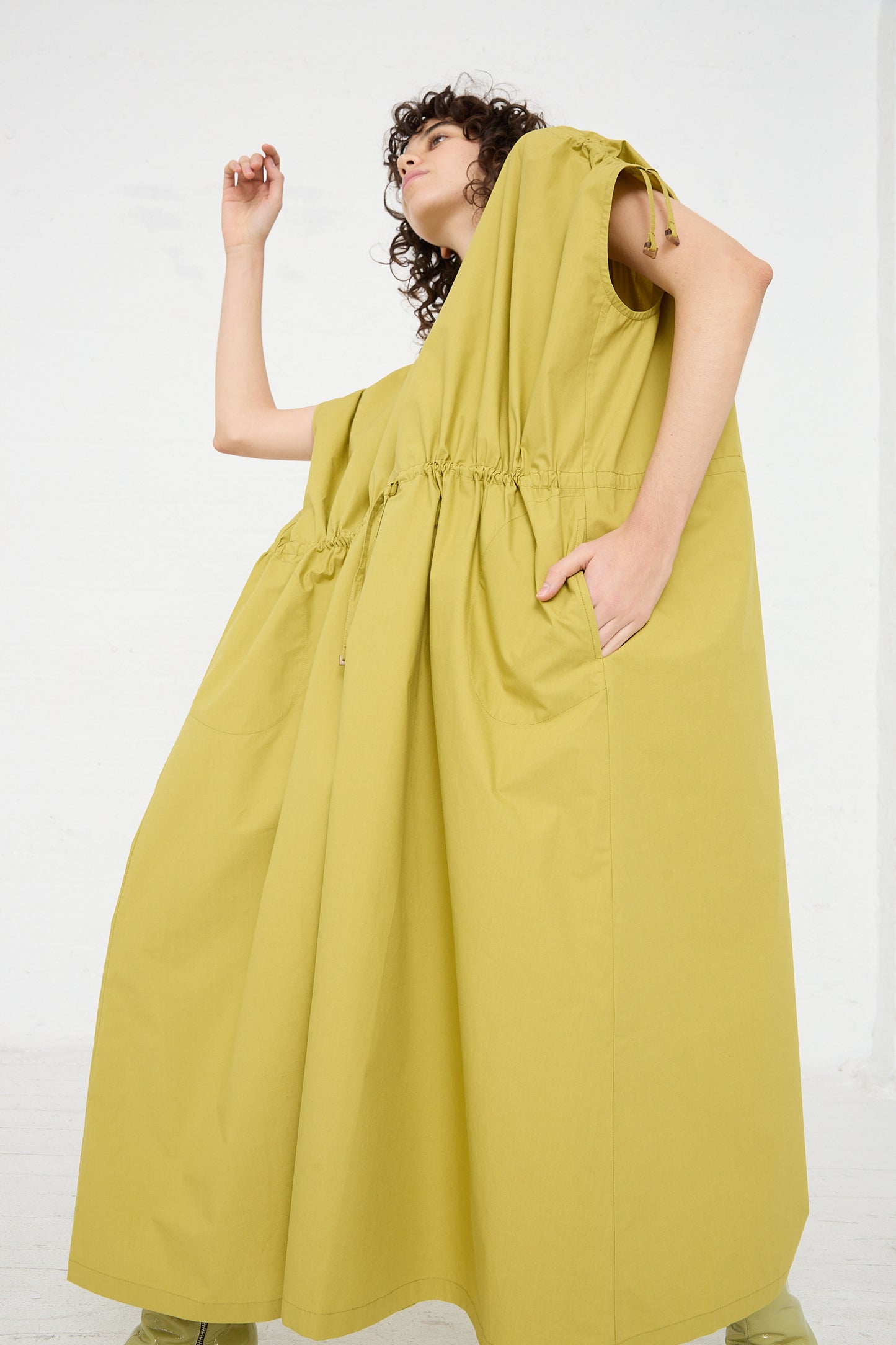 A woman in an oversized yellow Veronique Leroy Cotton Poplin Gathered Dress in Matcha is posing in a white room.