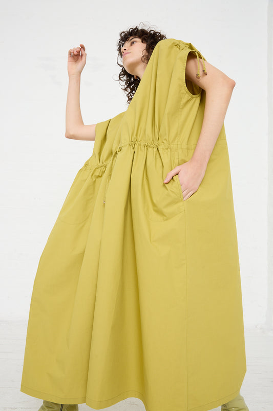 A woman in an oversized yellow Veronique Leroy Cotton Poplin Gathered Dress in Matcha is posing in a white room.