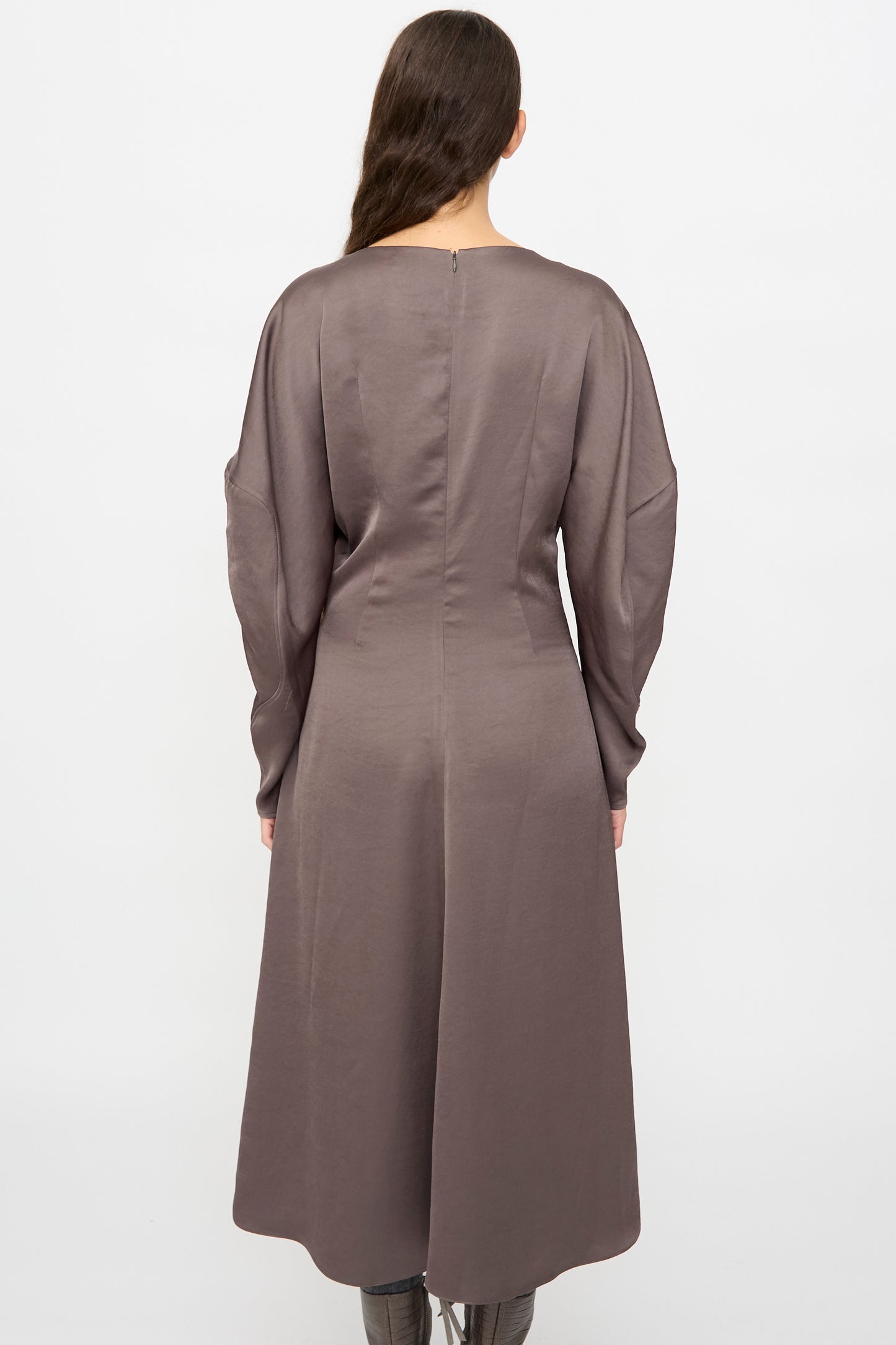 A person with long brown hair, facing away, wears the Veronique Leroy Dress with Scarf in Wood, featuring sculpted sleeves and a fitted waist, paired with tall boots against a plain white background.