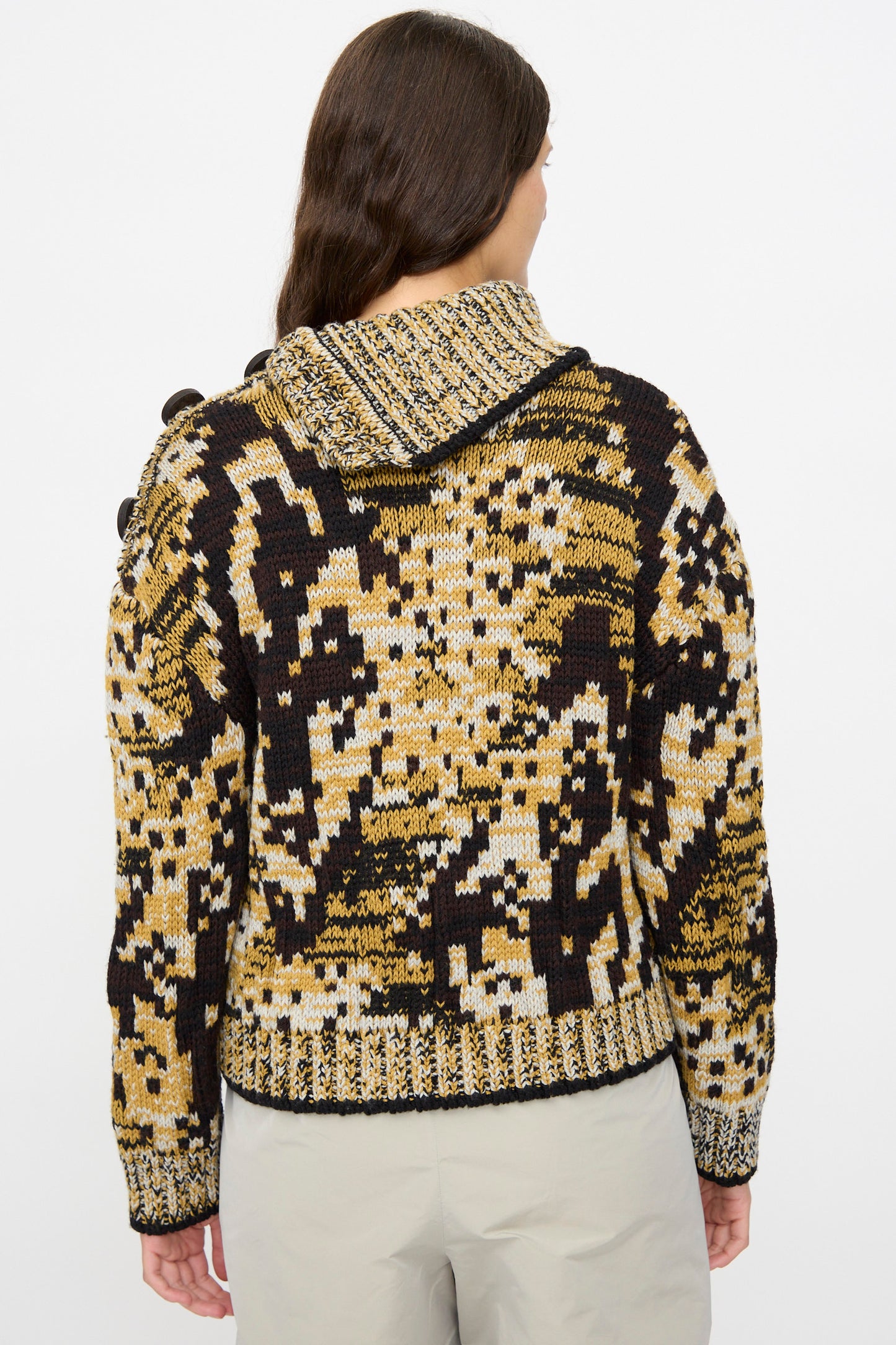 A person with long brown hair is seen from the back wearing Veronique Leroy’s Sweater in Sepia, a relaxed fit piece featuring a yellow, black, and beige abstract pattern.
