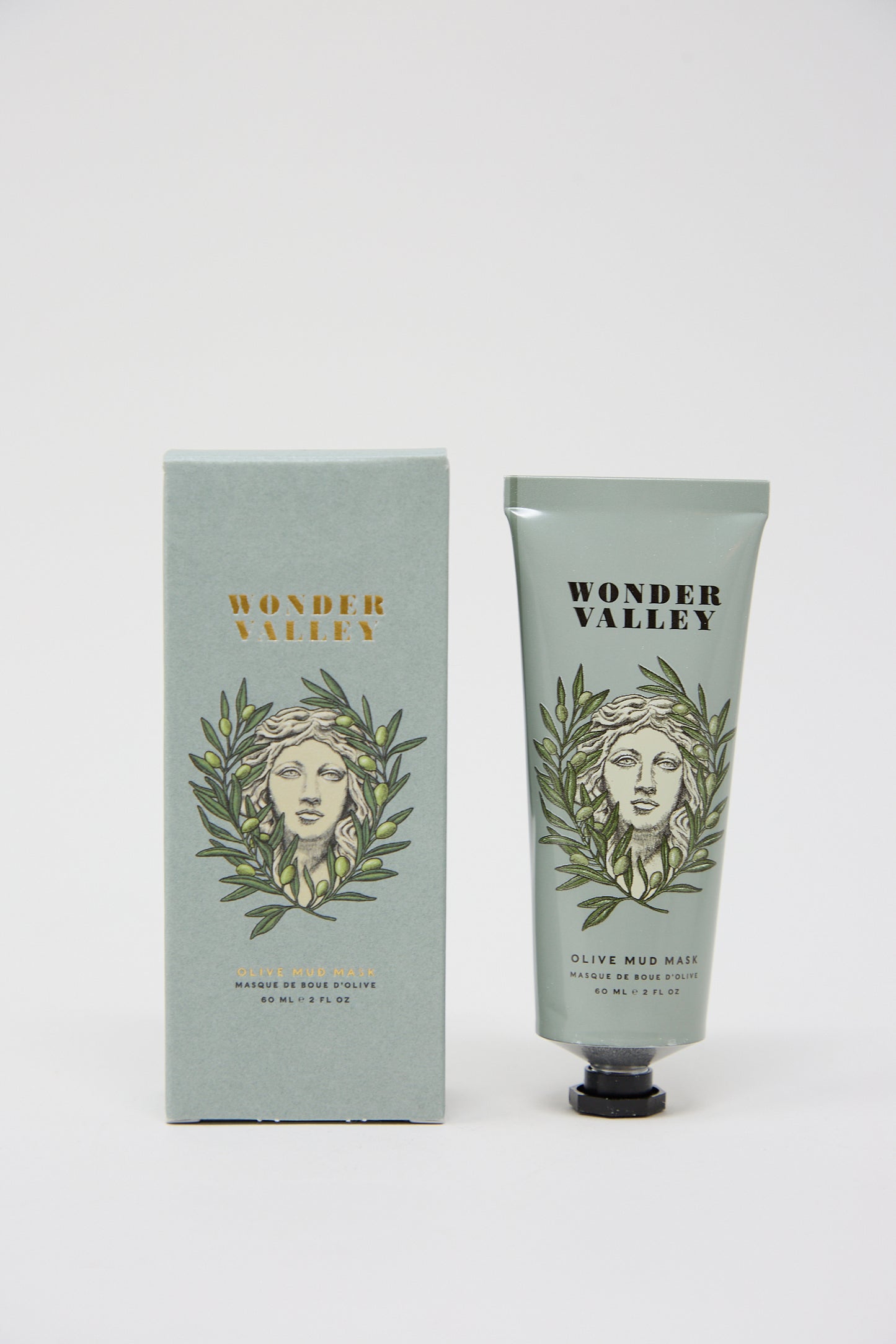 A tube of Wonder Valley Olive Mud Mask, which extracts impurities and prevents breakouts, next to its packaging, both featuring the same design of a woman's face surrounded by olive branches.