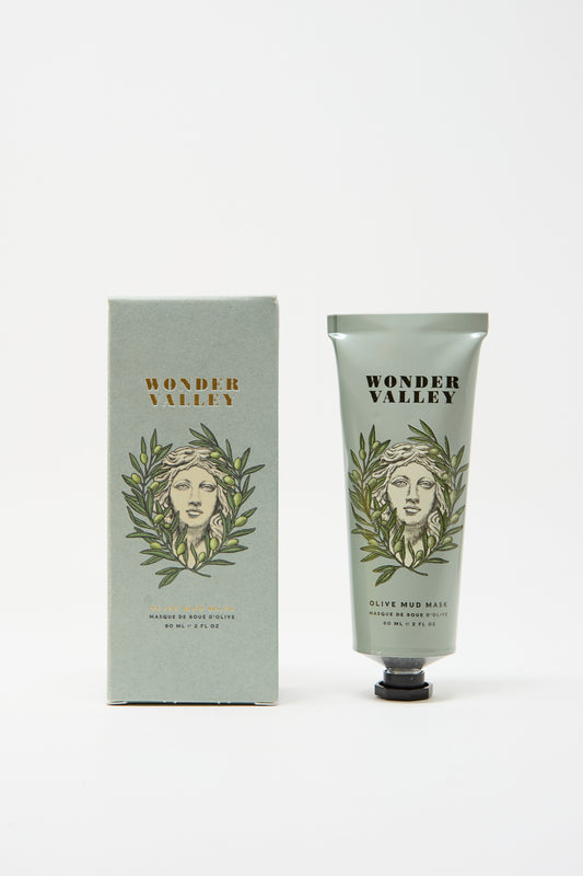 The Wonder Valley Olive Mud Mask is shown alongside its matching box, both featuring an illustrated face with olive branches on a light green background. This mask hydrates and balances skin for a refreshed look.