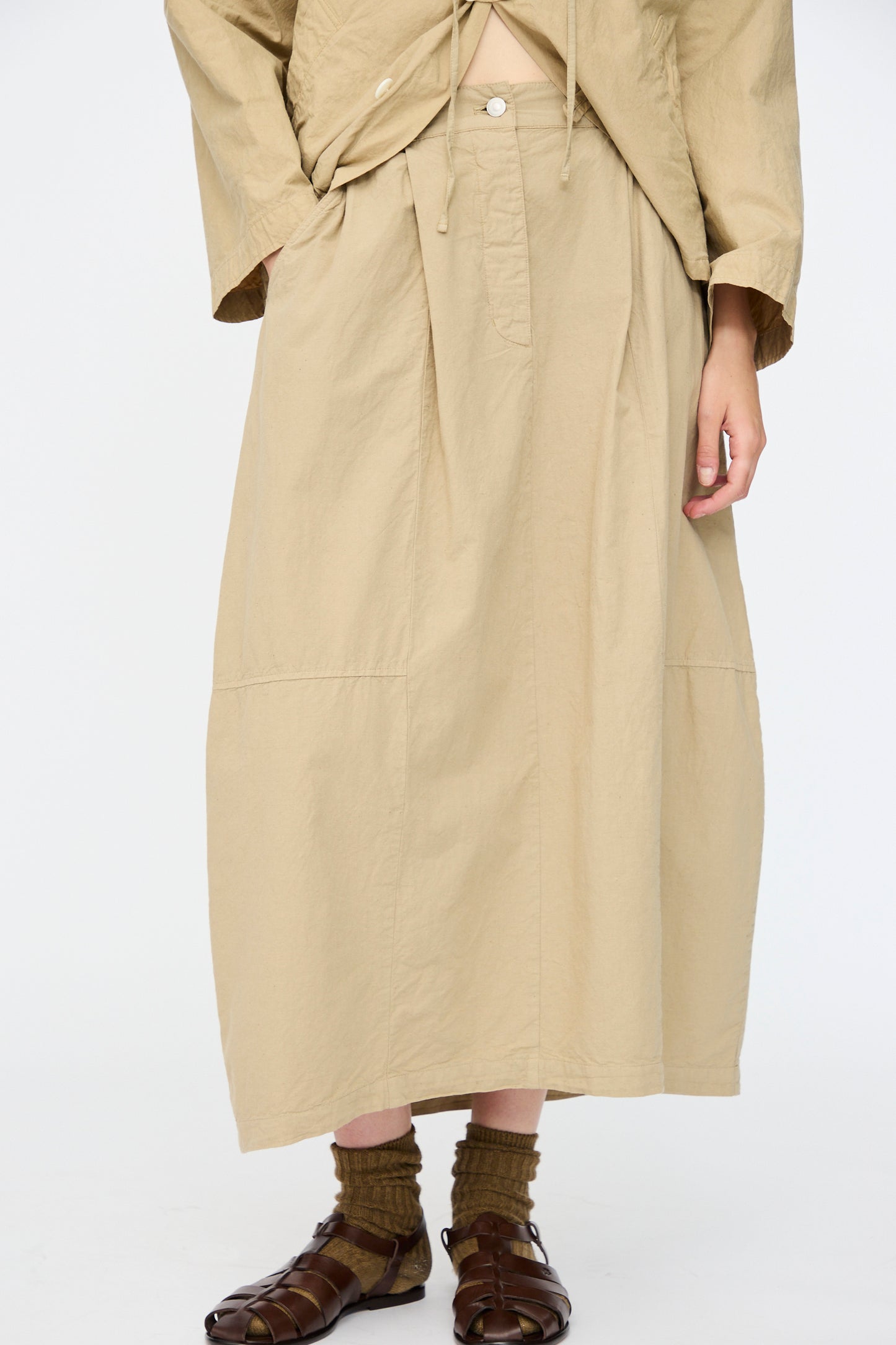 A person stands against a plain white background wearing nest Robe's Cotton Linen Dungaree Balloon Skirt in Beige, paired with a matching top, brown socks, and brown sandals for a relaxed fit.