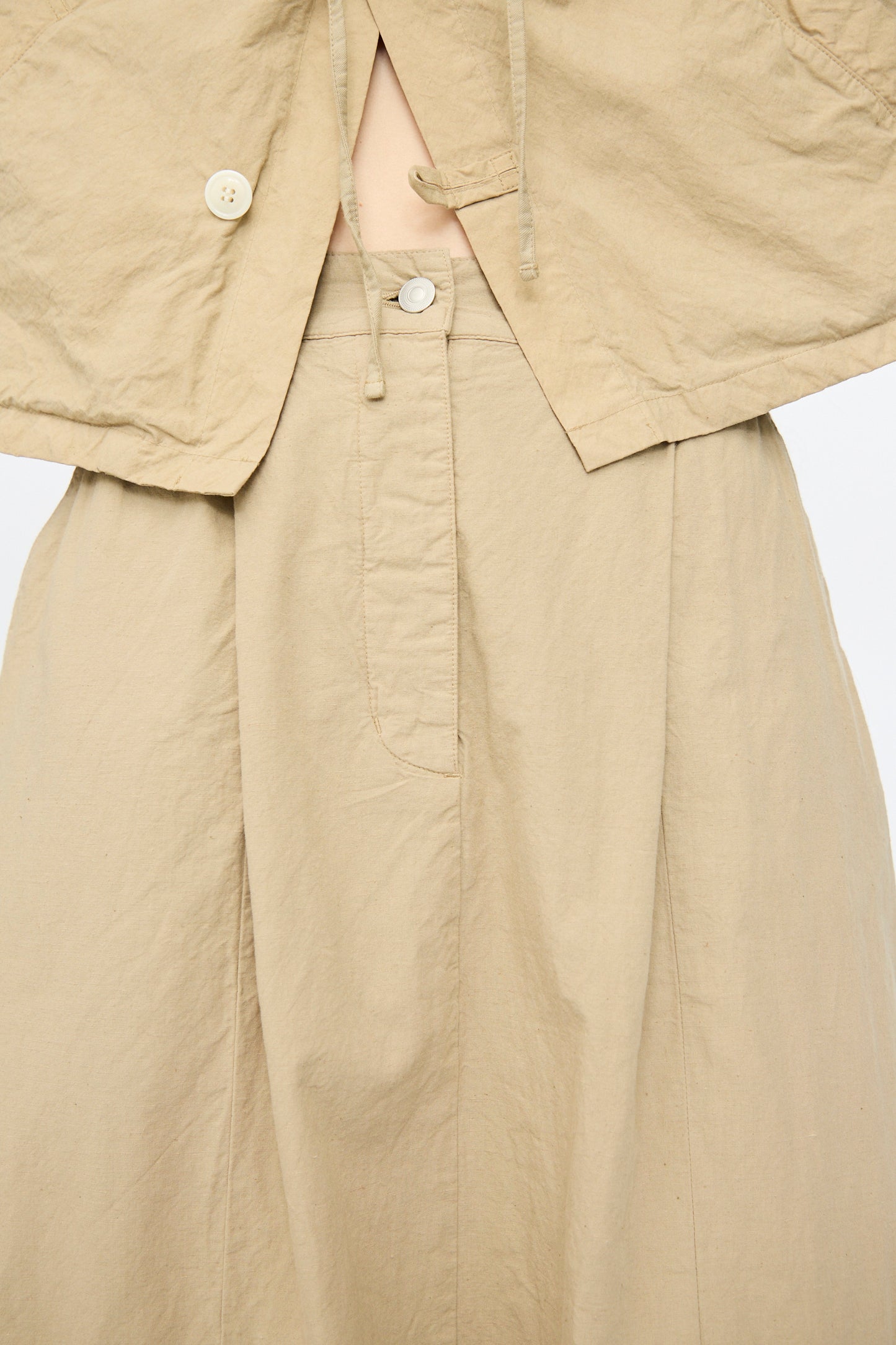 Close-up of a person wearing the nest Robe Cotton Linen Dungaree Balloon Skirt in Beige, styled with a matching beige top featuring fabric ties and visible buttons.