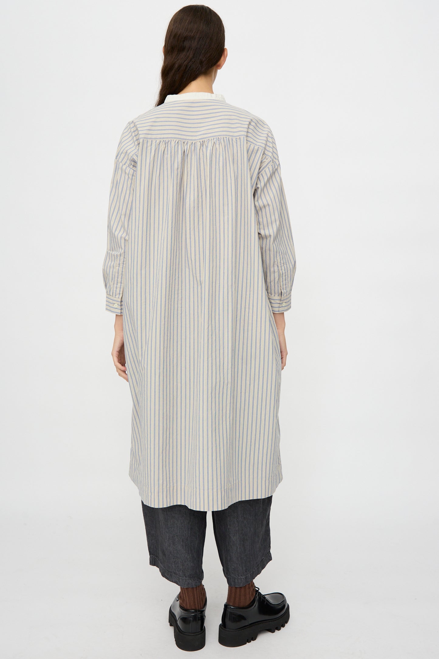 Person wearing the Cotton Pull-on Dress in Stripe by nest Robe, shown from the back with dark cropped pants and black shoes, standing against a plain white background.