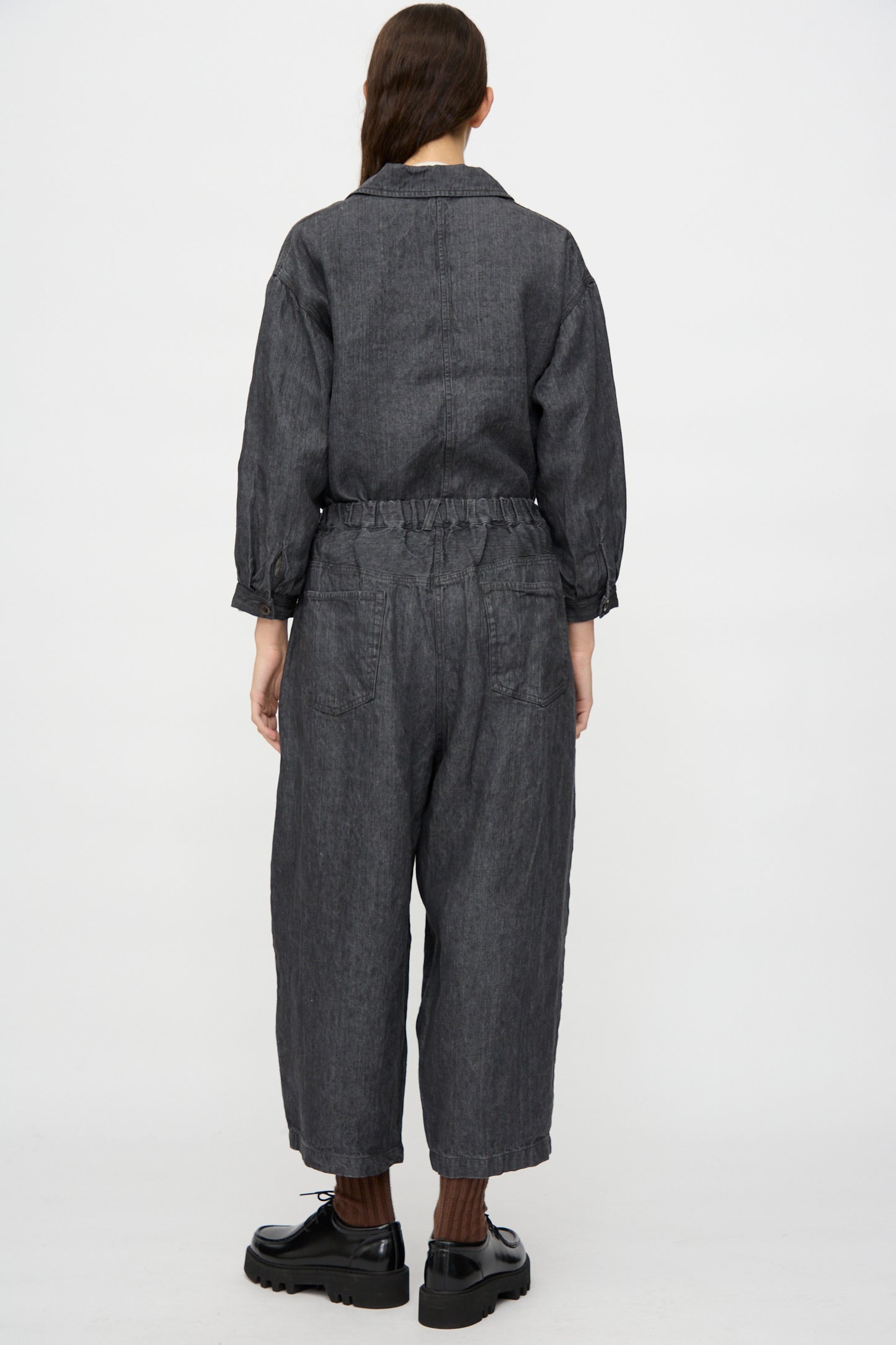 Person stands facing away, wearing nest Robe's Linen Denim Wide Pants in Black with black platform shoes and brown socks. Hair is tied back in a low ponytail. Made in Japan. White background.