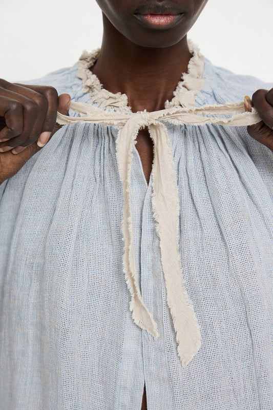 A person ties a bow on the neckline of a Linen Panama Weave Bolero Blouse in Light Blue from nest Robe.