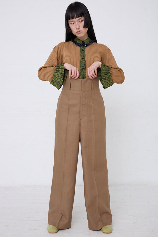 Young woman in a stylish TOGA ARCHIVES brown blouse with puff sleeves and TOGA ARCHIVES high waist trousers made from woven rayon blend, posing against a white background.