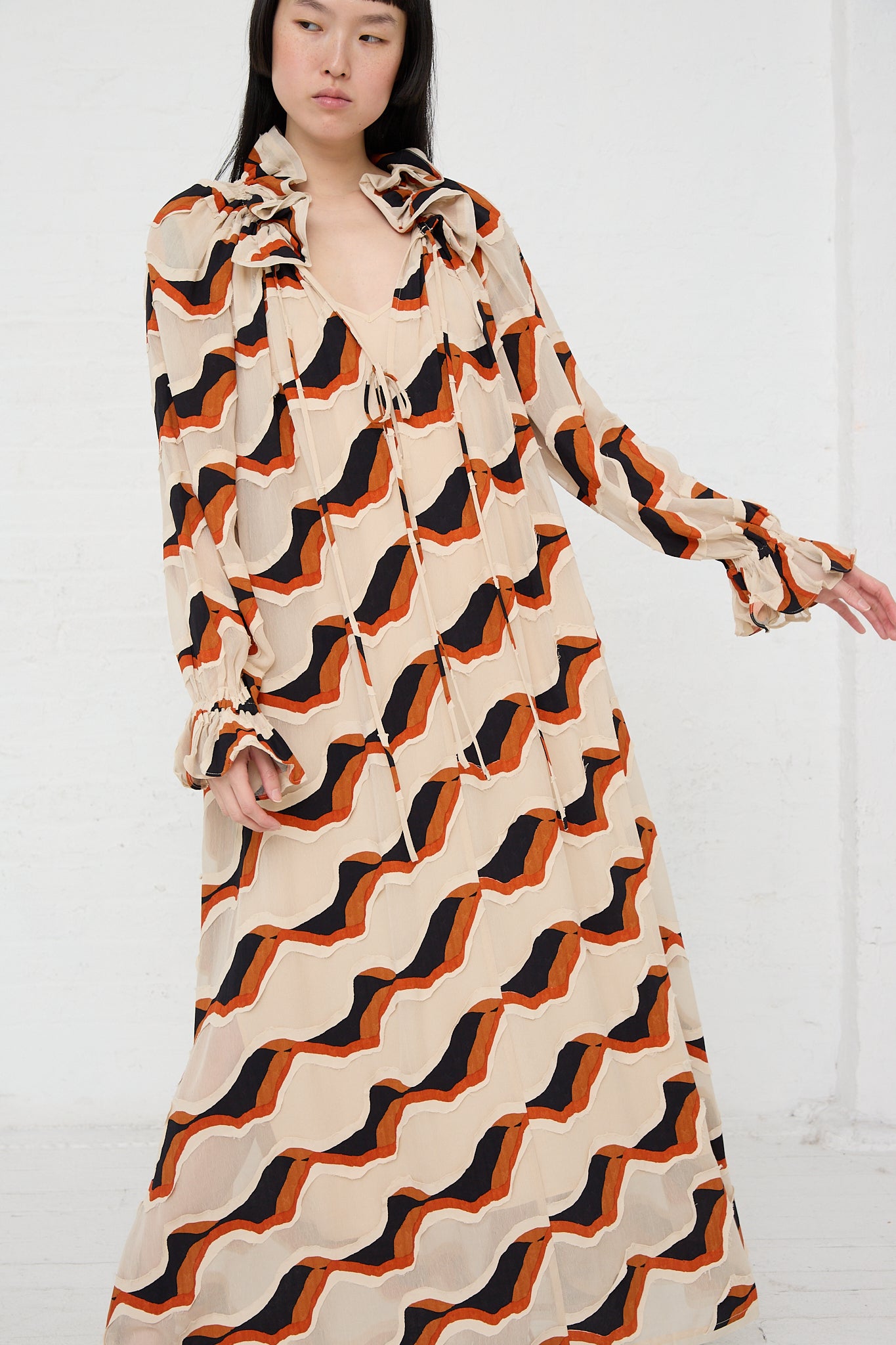 The model is wearing an Ulla Johnson Echo Dress in Conch with a black and orange pattern.