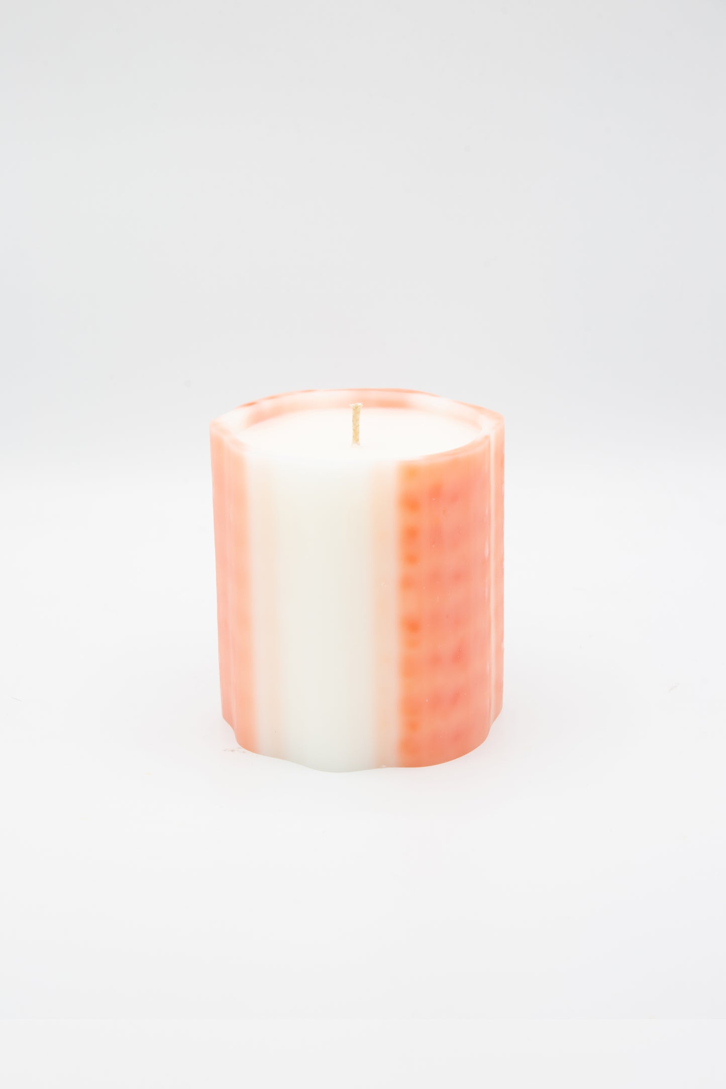 An Artisanal Candle in Neroli scent by Le Feu De L'eau. Candle is in a pink and white stripes wax vessel.