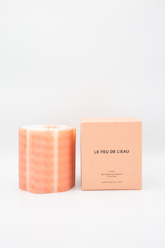 A pink colored Artisanal wax Candle in Neroli scent by Le Feu De L'eau, next to a pink box.