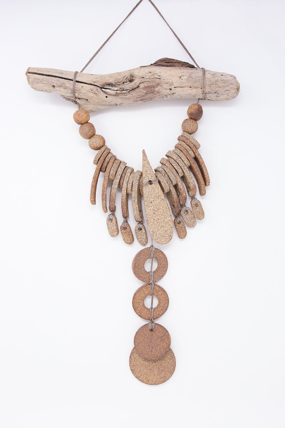 The Teardrop and Circle Wall Hanging in Mixed Brown by Heather Levine, handmade in California, showcases a cascading design of driftwood and metal ornaments, elegantly suspended by twine against a plain white background.