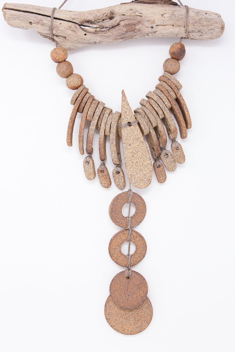 The Teardrop and Circle Wall Hanging in Mixed Brown by Heather Levine is a rustic piece handmade in California, featuring textured stone and wood elements hanging from a piece of driftwood.