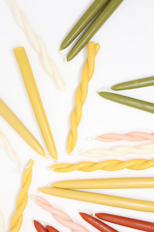 Assorted Hand Twisted Beeswax Candles in Mother's Milk and various colors, shaped and arranged in a pattern on a white background by Wax Atelier.