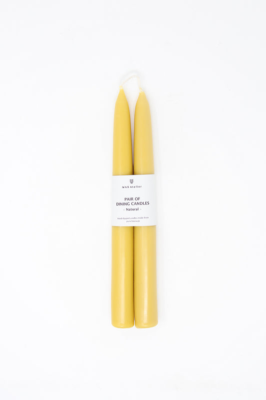 A pair of yellow Wax Atelier Beeswax Dining Candles in Natural against a white background.