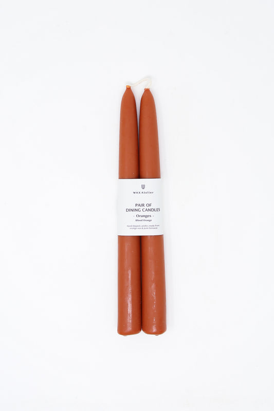 Two terracotta Blood Orange beeswax dining candles from Wax Atelier with packaging label against a white background.