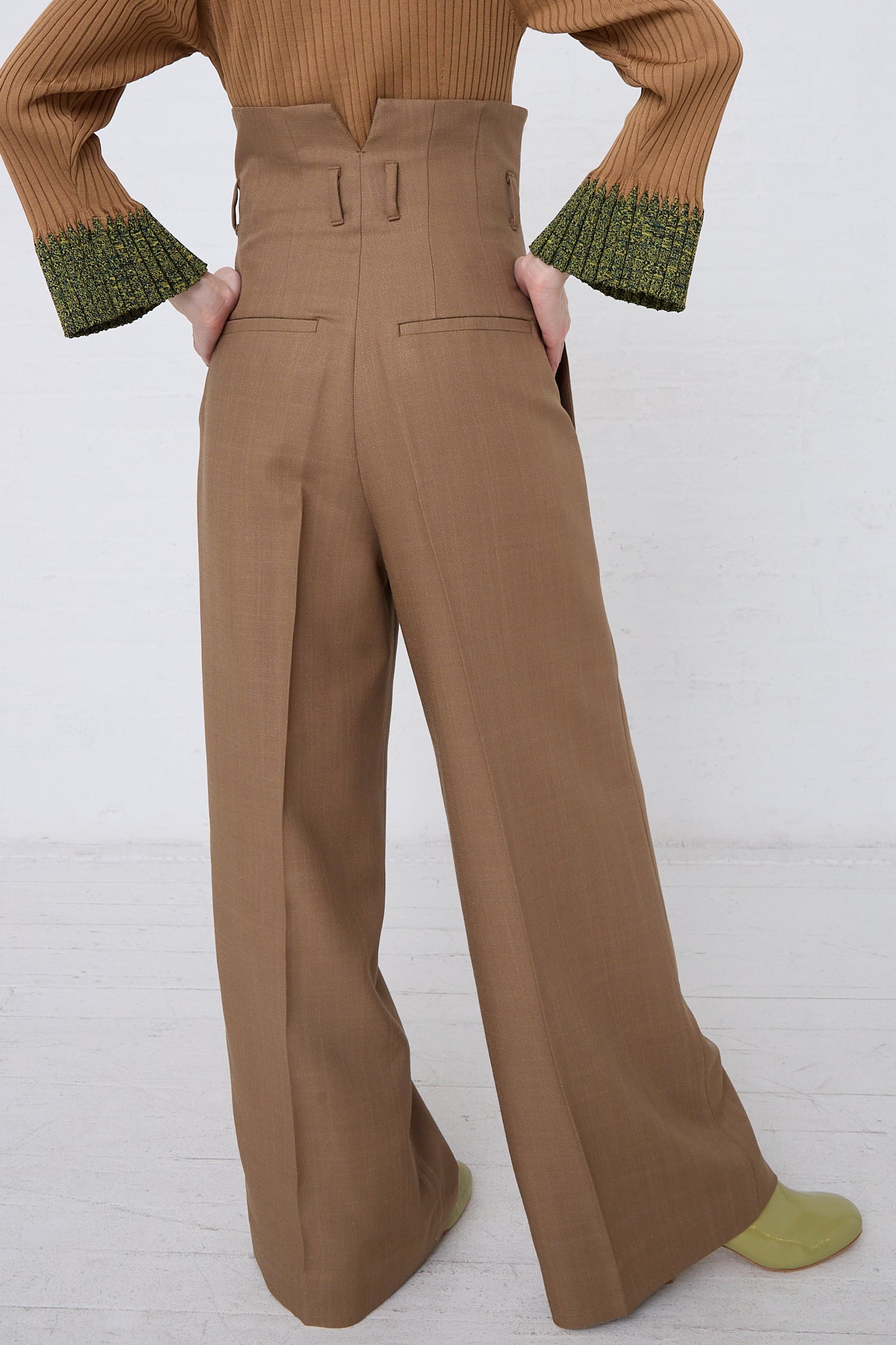 A person wearing high-waist TOGA ARCHIVES trousers in brown.