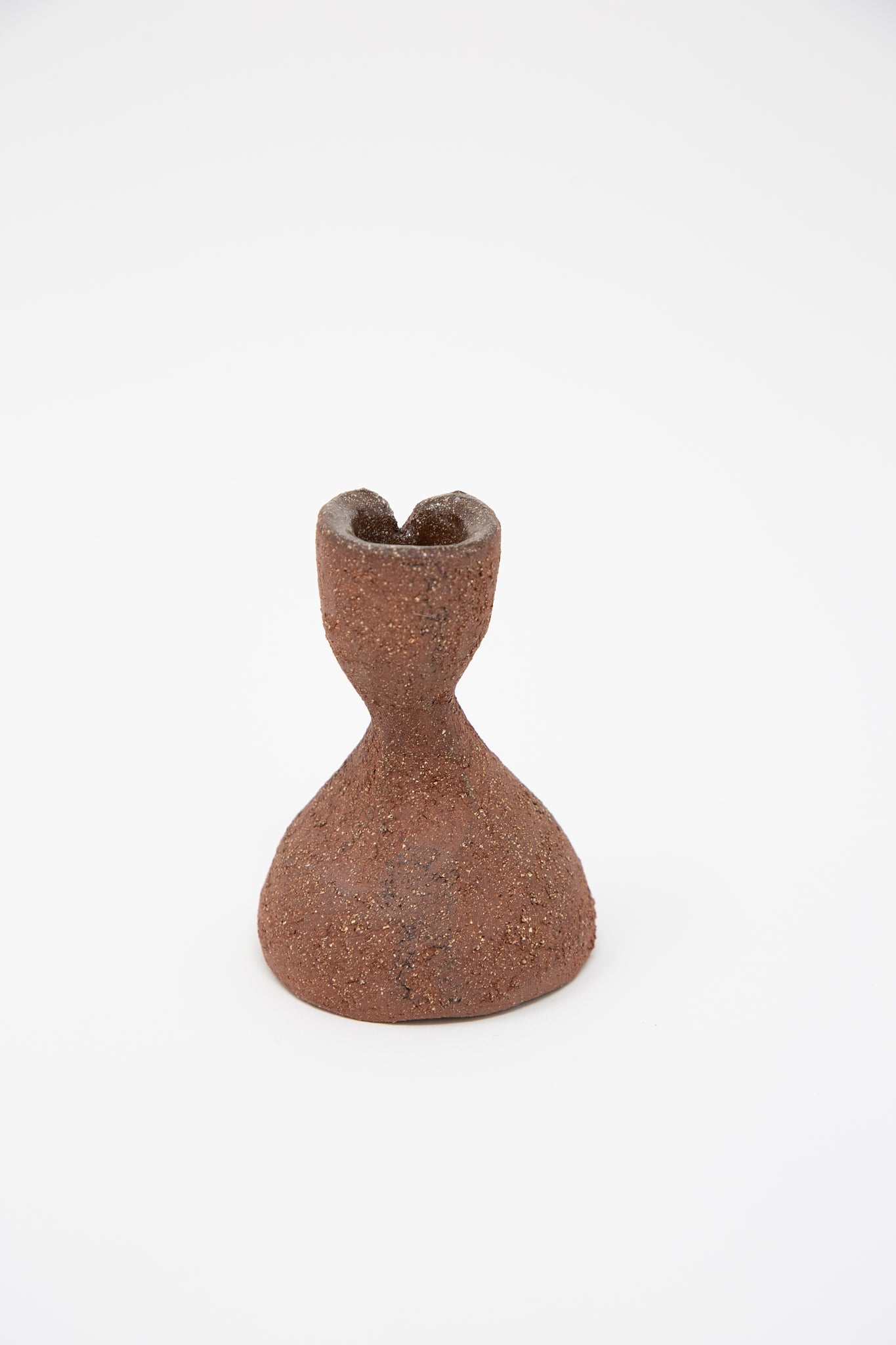 A petite, hourglass-shaped Hand Built Candlestick in Terracotta Sculpture Clay with a textured surface and a hollow top opening, from the brand Lost Quarry, set against a plain white background.