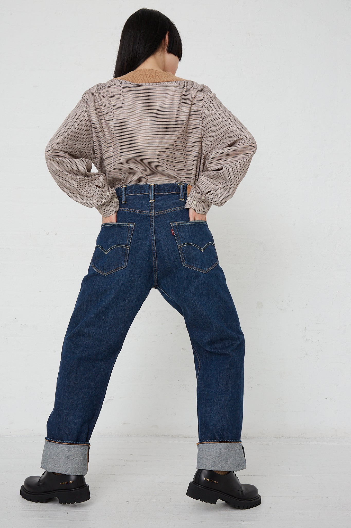 A woman wearing a pair of Bless No. 75 SMLXL Readymade Vintage Levis in Dark Blue jeans posing in front of a white wall.
