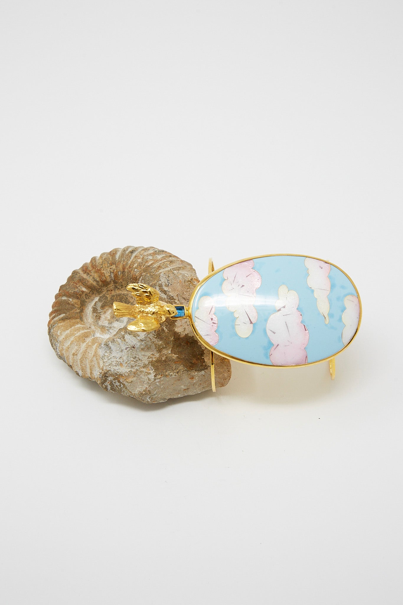 A blue and white enamel bracelet in Clouds with Bird by Sofio Gongli on a rock. Side view.