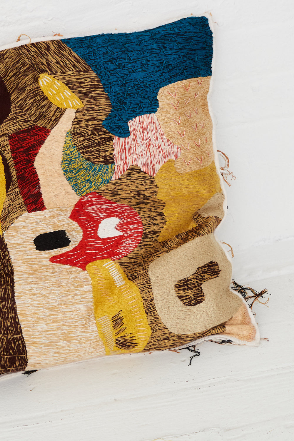 A Complex Embroidery Cave Cushion by Luna Del Pinal with a colorful hand embroidery design on it.