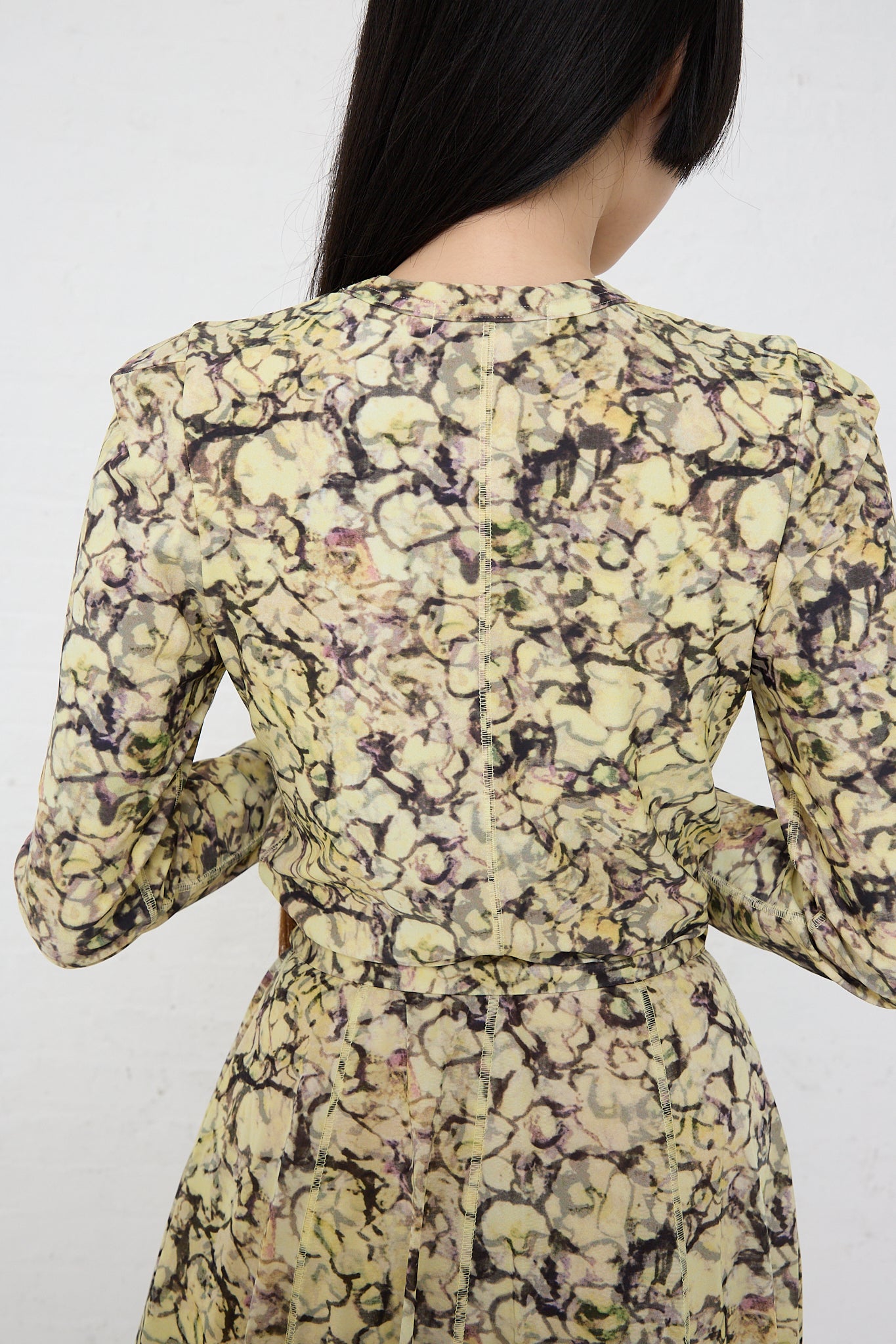 Rear view of a woman wearing a TOGA ARCHIVES Tricot Print Dress in Yellow with a fitted waist and long sleeves, standing against a plain white background.
