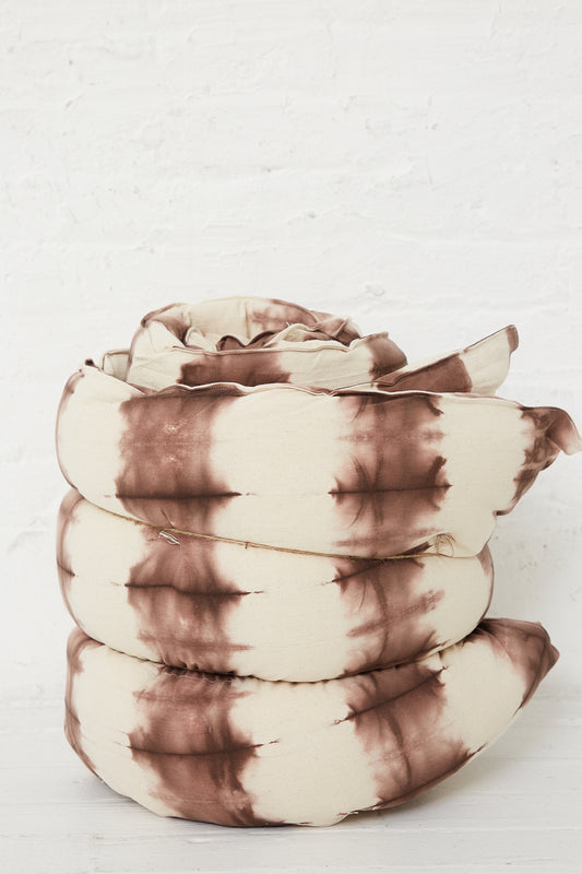 A Tufted Overlay Mattresses in Chocolate Tie Dye by Tensira in front of a white brick wall.