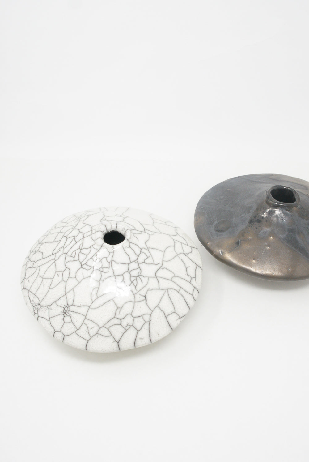 Two Ikebana Vases in Raku-Fired Stoneware with knob tops on a white background, one with a crackled glaze finish, the other with a glossy dark glaze by MONDAYS.