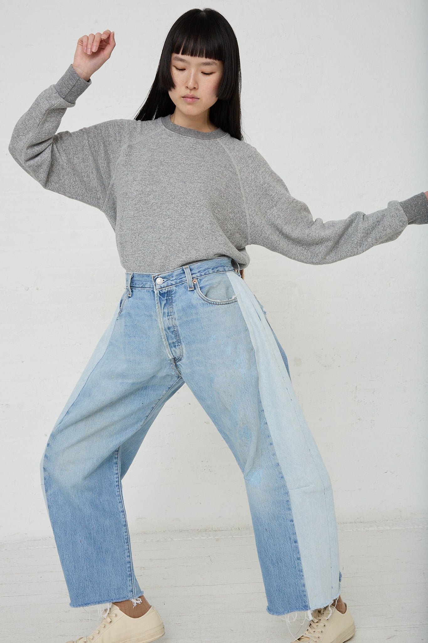 A woman wearing a grey sweater with the B Sides Lasso Jean in Vintage Indigo denim jeans. Front view and full length.