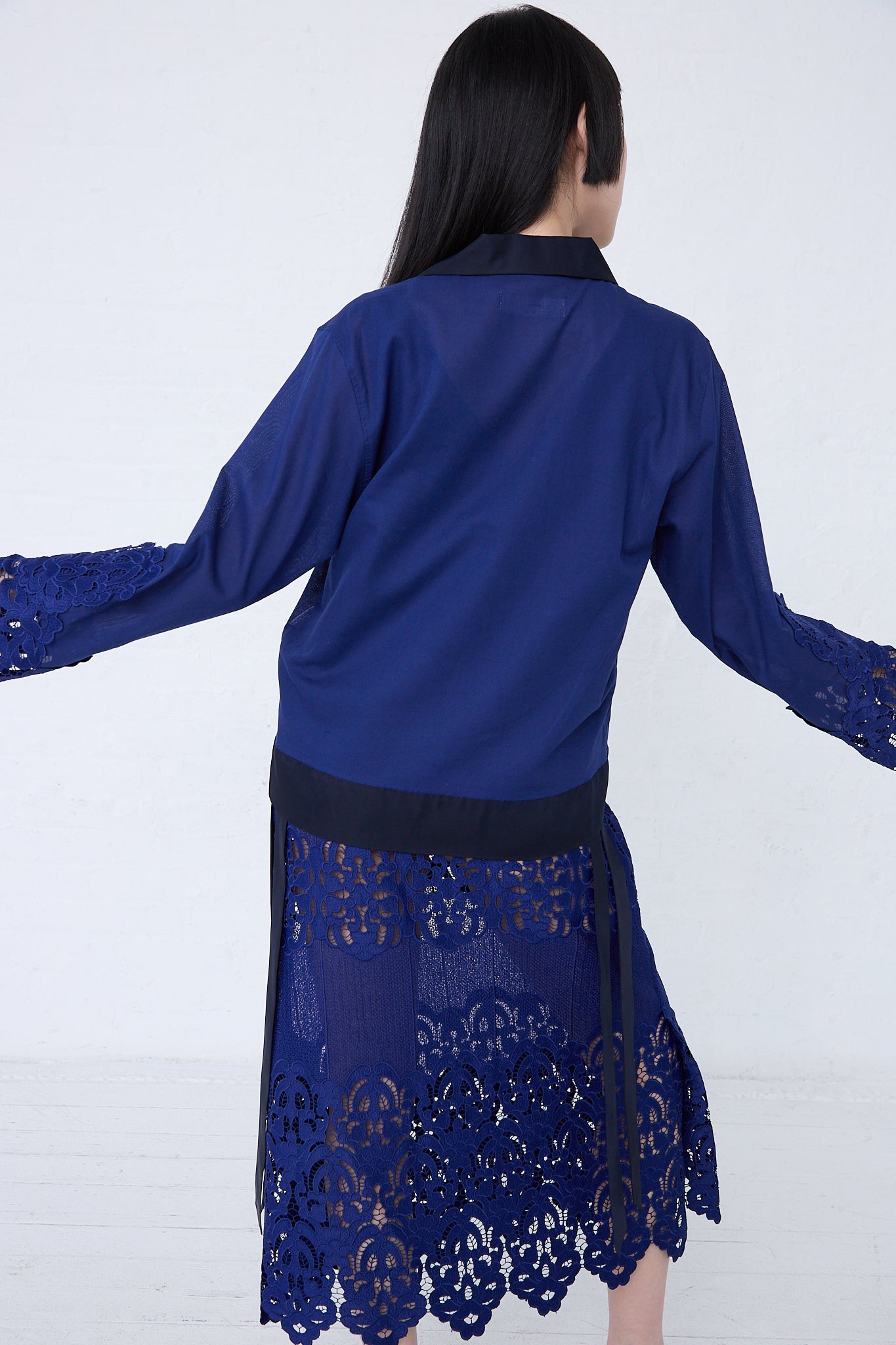 A woman from behind, wearing a TOGA ARCHIVES Mesh Lace Shirt in Blue with relaxed fit detailing at the bottom, standing against a white background.