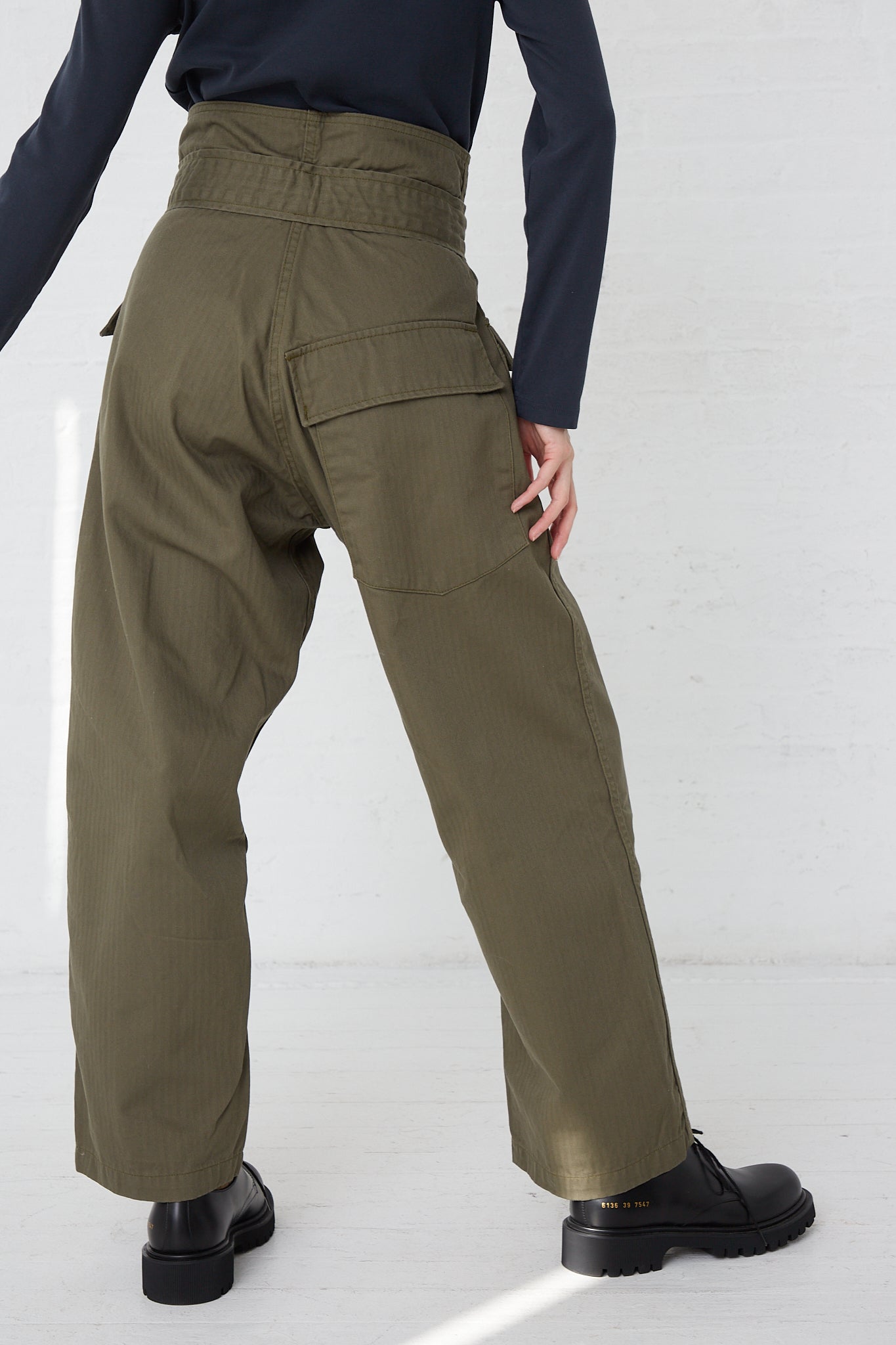 A woman in As Ever's Olive Tie Tanker pants and a black turtle neck. Back view.