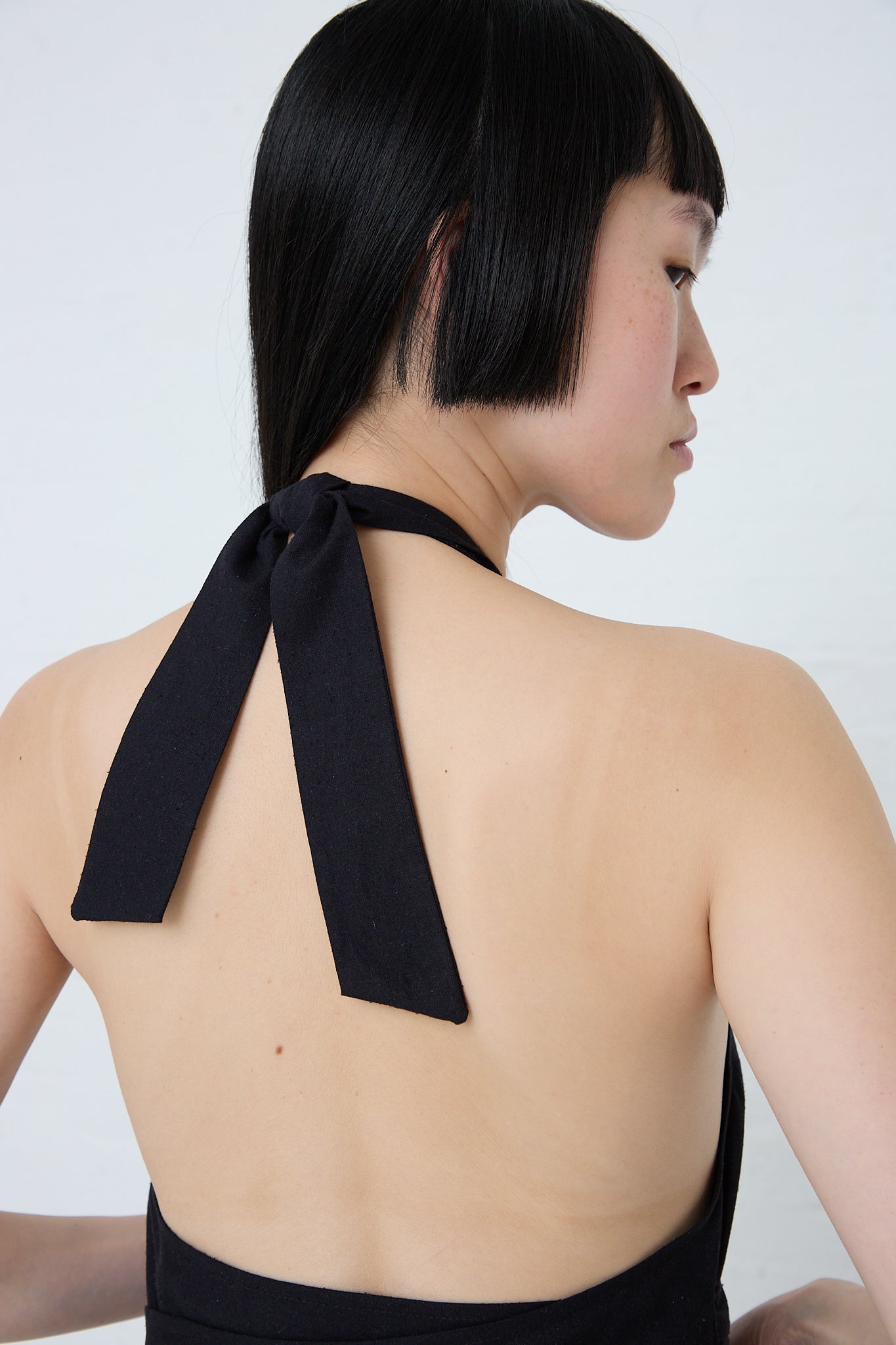 The back view of a woman wearing a Baserange Wild Silk Trope Apron Dress in Black sustainably produced.