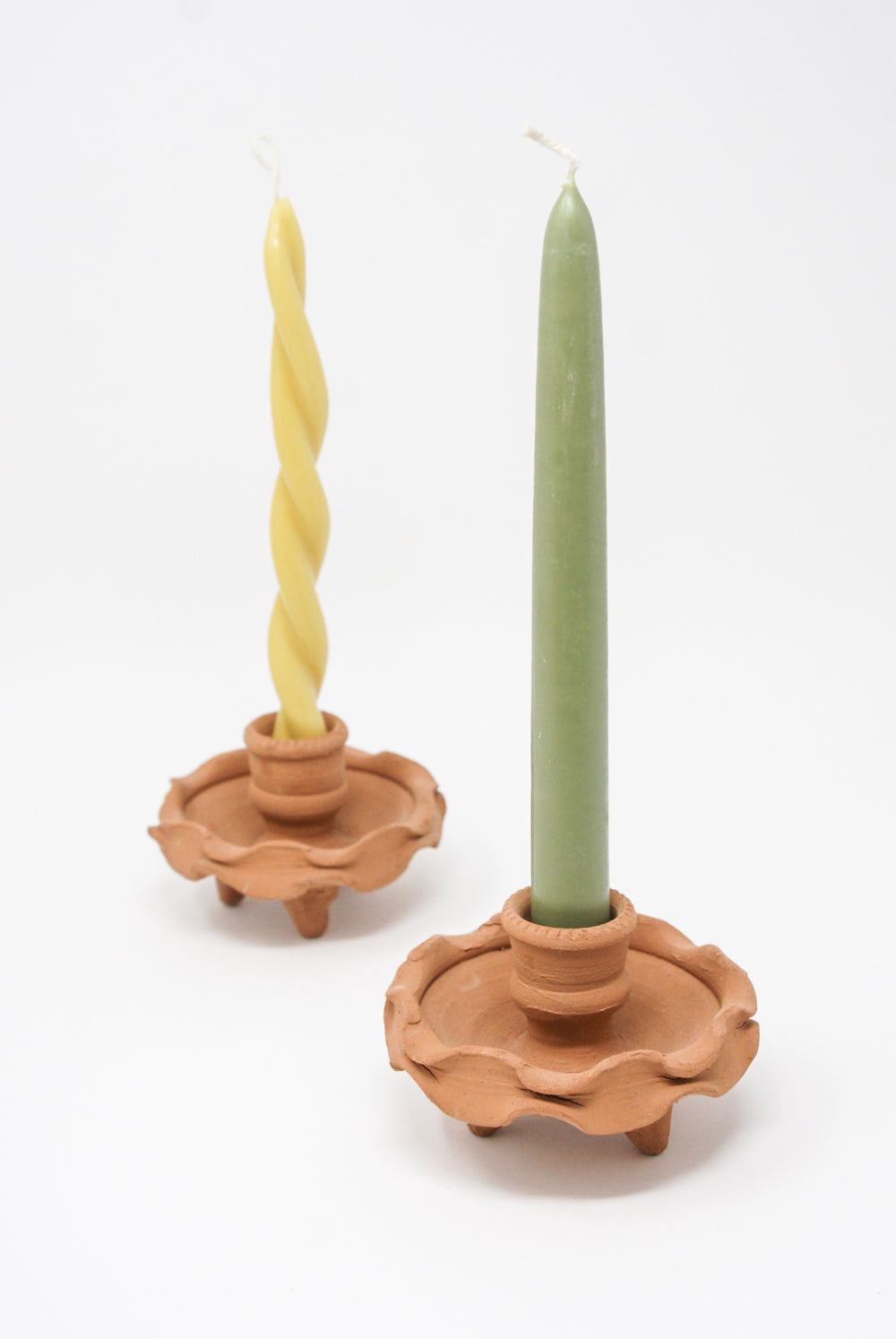Two Beeswax Dining Candles in Moss holders, one twisted and made of beeswax, the other straight with green tea wax and matcha aroma, against a white background. From Wax Atelier.