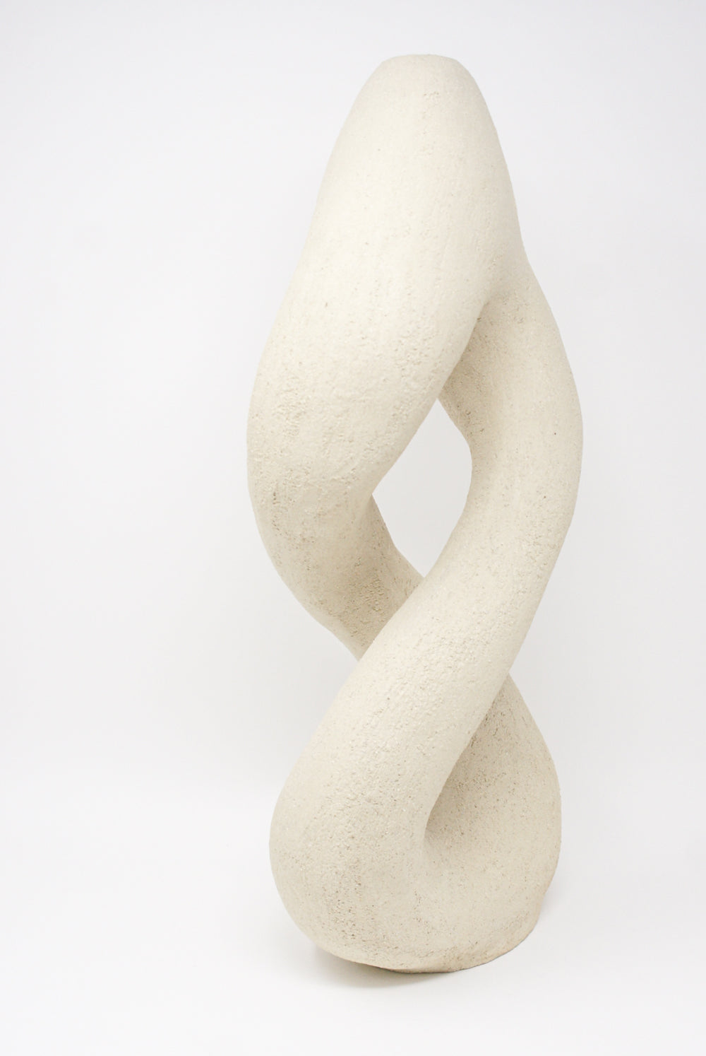 Hand Built Vessel No. 000395 by Lost Quarry is an abstract sculpture featuring a twisted, looped design, crafted from a textured light beige material that emulates the look of a hand-built vessel, standing against a plain white background.