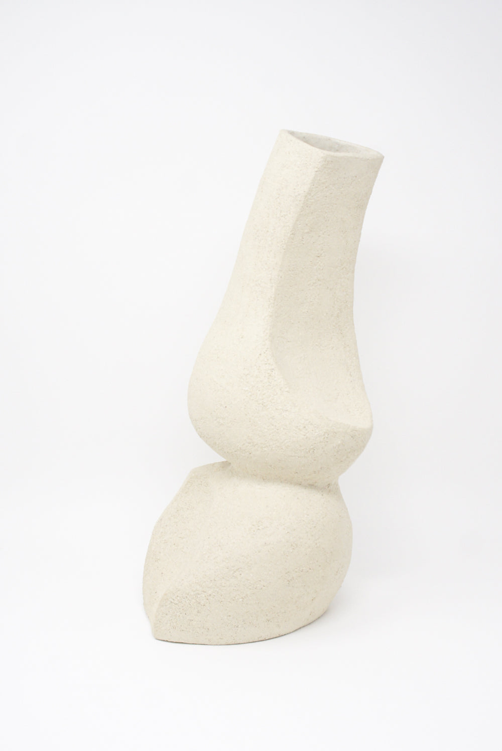 On a pristine white background stands the Hand Built Vessel No. 000345 by Lost Quarry, a uniquely shaped ceramic vase with an abstract, curvilinear design. This hand-crafted piece boasts a textured surface and a narrow opening at the top, making it ideal for floral arrangements.