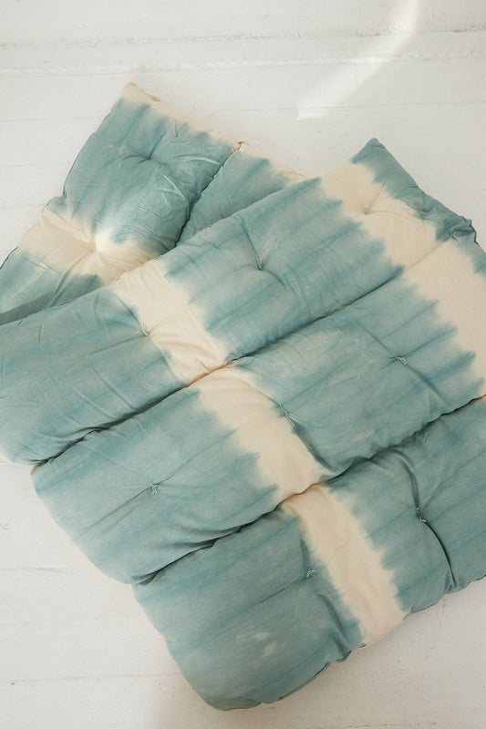 A sustainable Tufted Overlay Mattress in Celadon Green Tie Dye by Tensira on a wooden floor.
