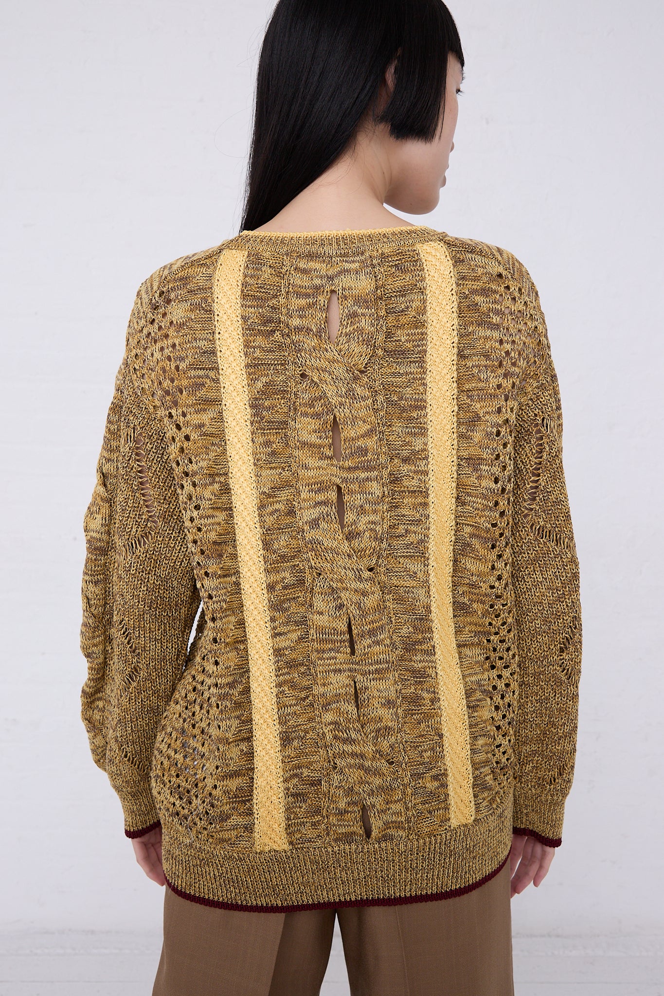 Woman from behind wearing a TOGA ARCHIVES Mesh Knit Pullover in Yellow with ribbon details along the spine, standing against a plain white background.