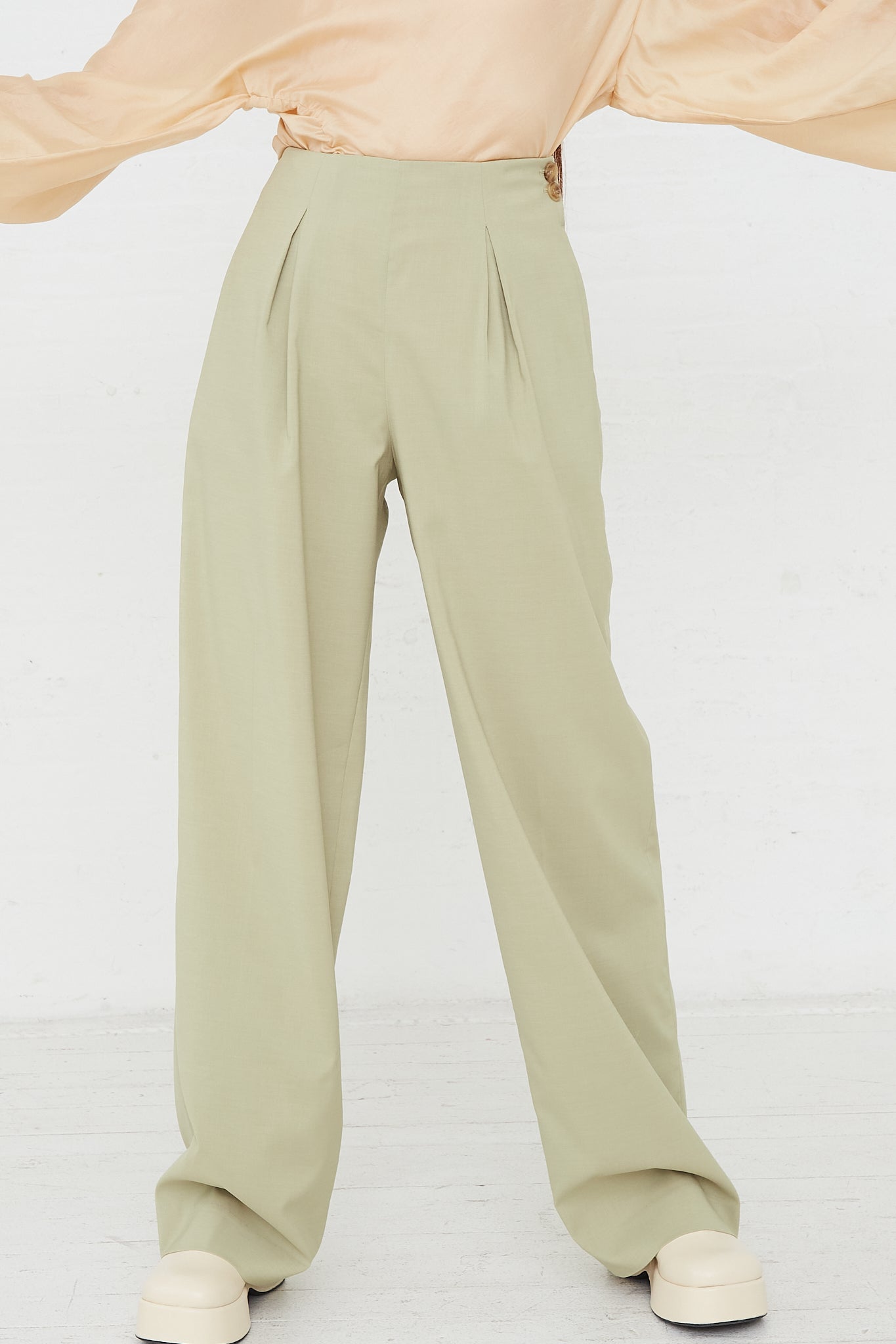 A woman wearing Rejina Pyo's Reine Trouser in Sage, a minimalist trousers made of a sage green polyester silk blend. Front view.