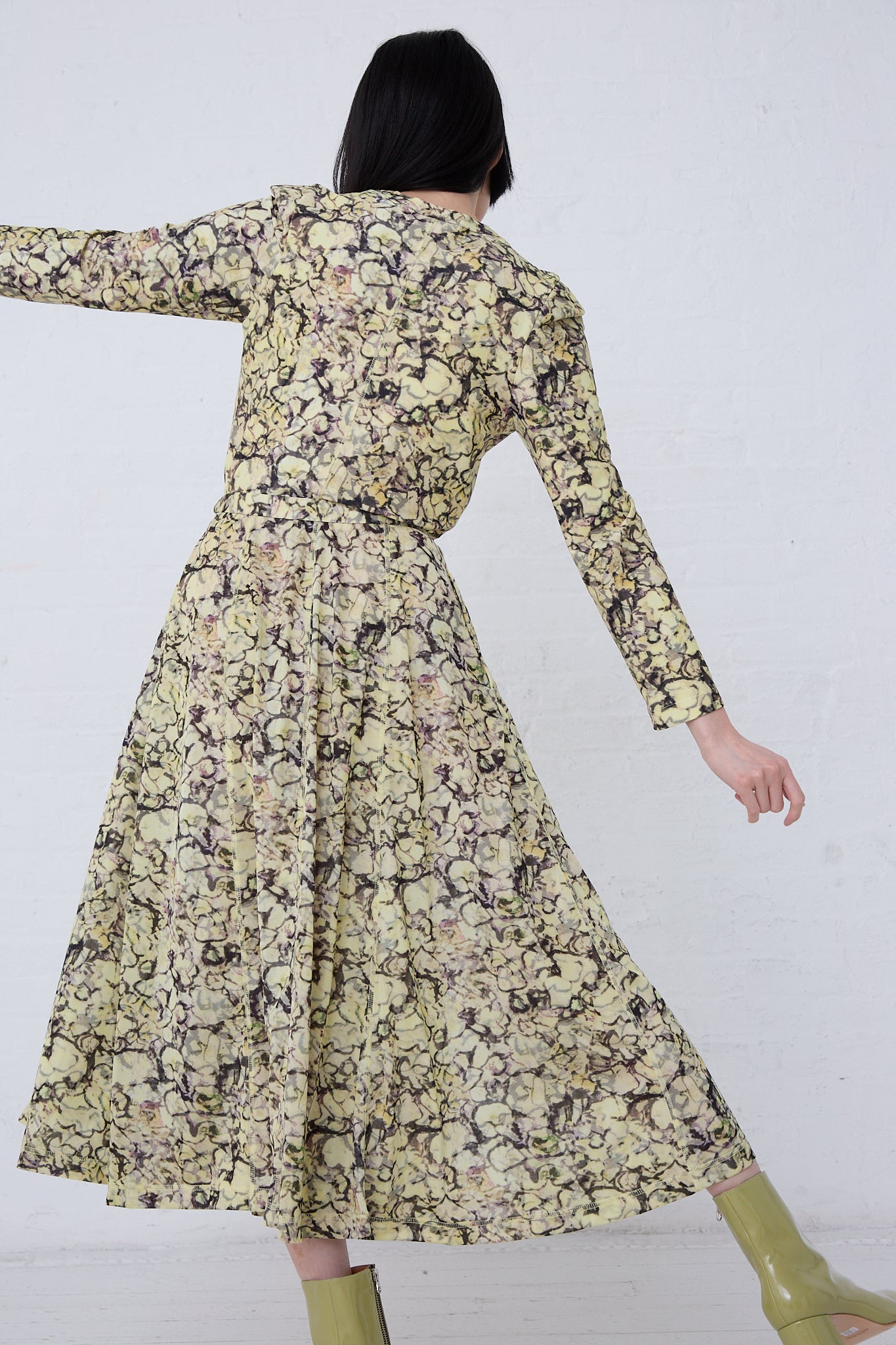 Rear view of a woman in a TOGA ARCHIVES Tricot Print Dress in Yellow twirling, revealing the design of the back and the flow of the skirt, against a white background.