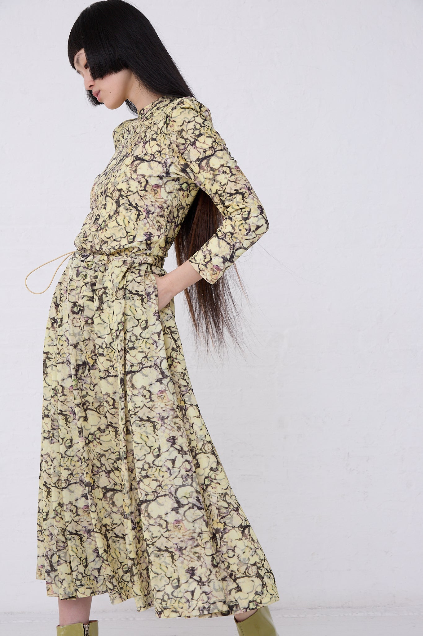 Woman in a TOGA ARCHIVES Tricot Print Dress in Yellow and high ponytail posing sideways against a white backdrop.