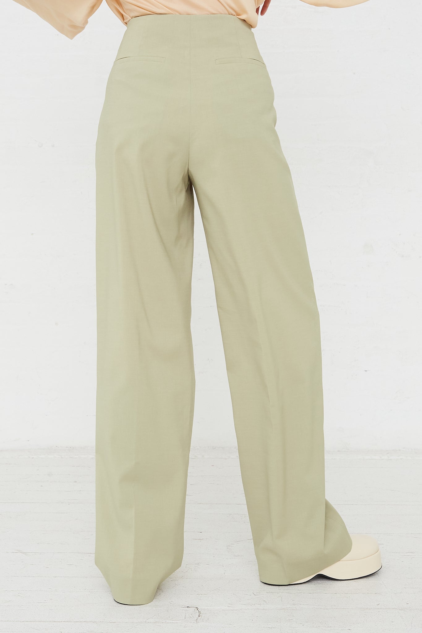 The back view of a woman wearing Rejina Pyo's Reine Trouser in Sage, in a minimalist style.