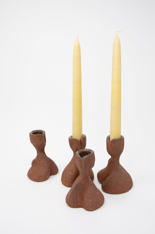 Four Hand Built Candlesticks in Terracotta Sculpture Clay by Lost Quarry, each featuring a unique brown abstract design, displayed on a white background. Two of the candlesticks hold tall, unlit yellow candles. Their handmade and textured nature adds an artisanal touch to any setting.