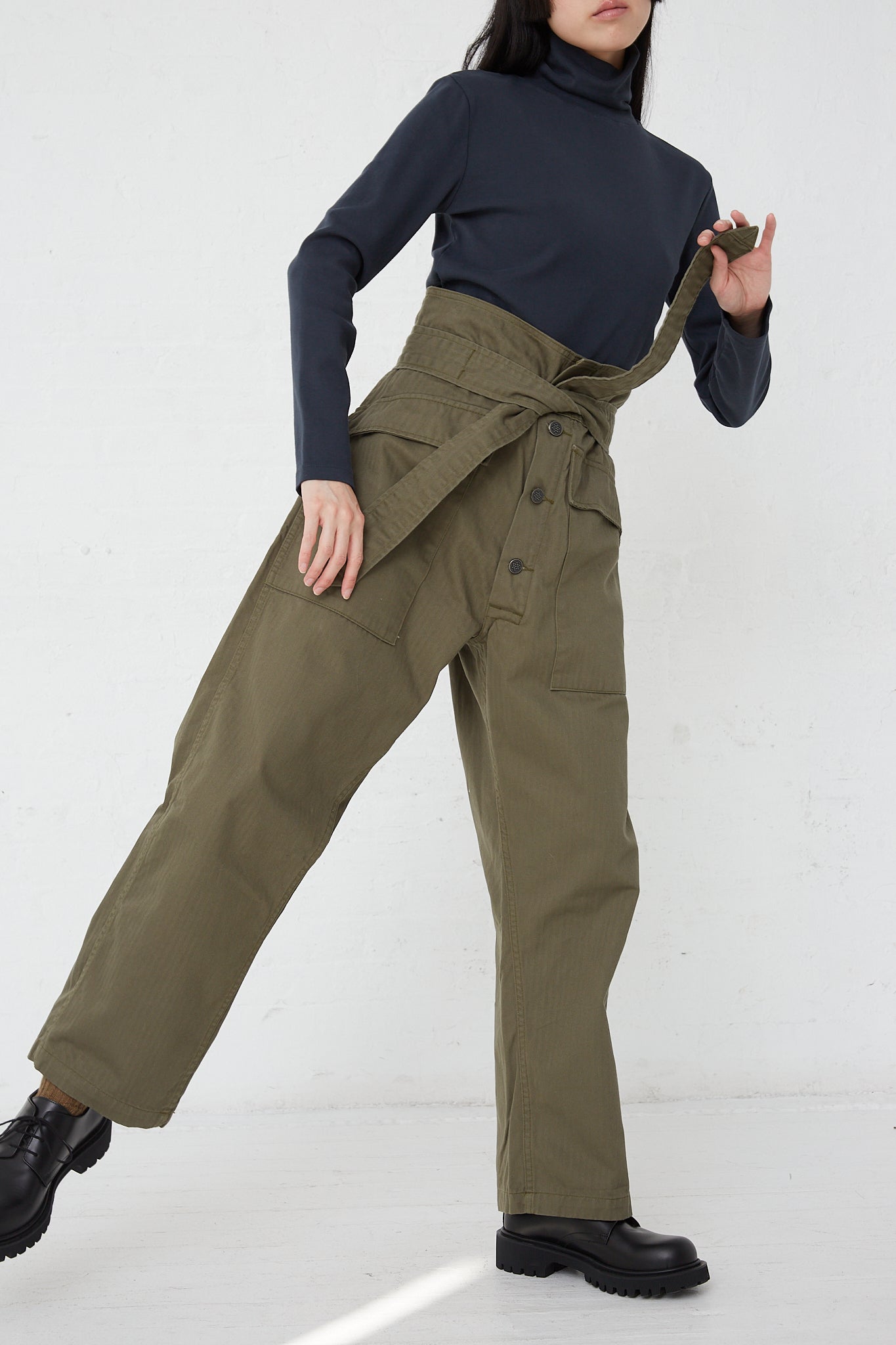 A woman wearing the As Ever Tie Tanker in Olive and a black turtleneck made of 100% cotton.