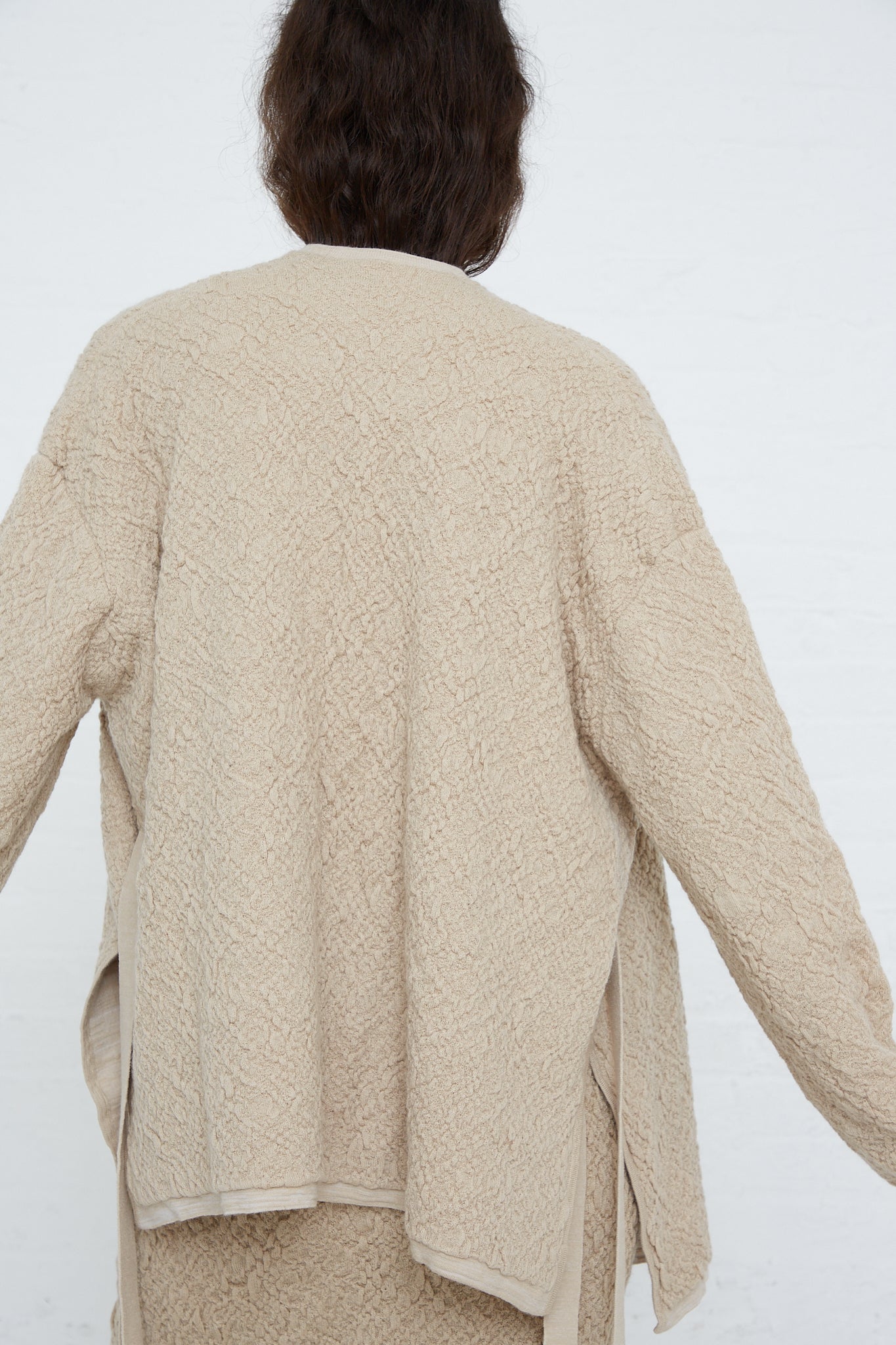 The back of a woman wearing an open Lauren Manoogian Alpaca Gauze Cardigan in Antique made from sustainable knit alpaca.