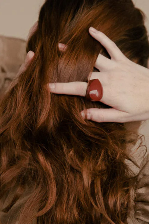 The back of a head of long deep red hair with fingers running through it - one finger has a deep red baubble ring by Kathleen Whitaker. Click here to read more.